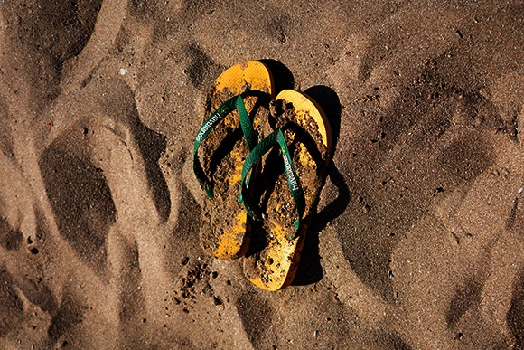 Fotografia aérea em estilo documental de um par de chinelos Havaianas amarelos com tiras verdes, cobertos de areia molhada na praia. Imagem usada para ilustrar o conceito de street marketing e marketing branding no artigo da agência Quel Chic.