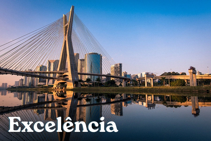 Vista da Ponte Estaiada Octávio Frias de Oliveira ao entardecer, com o skyline de São Paulo refletido no rio Pinheiros, representando o valor de excelência da Quel Chic Agência